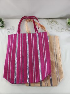 a set of vibrant potli bags, perfect for wedding gifts and bridal shower favors. The bags, adorned with silver stripes, come in a deep pink and a soft peach hue