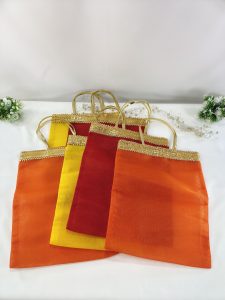 Elegant bridal silk potli bags in vibrant shades of orange, red, and yellow, embellished with golden lace handles, ideal for wedding favors and bridesmaid gifts. These handmade potli bags